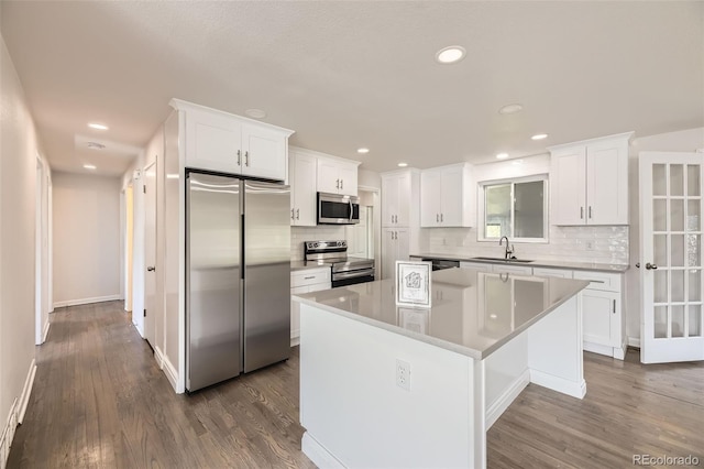 kitchen featuring stainless steel appliances, a sink, a kitchen island, tasteful backsplash, and white cabinetry