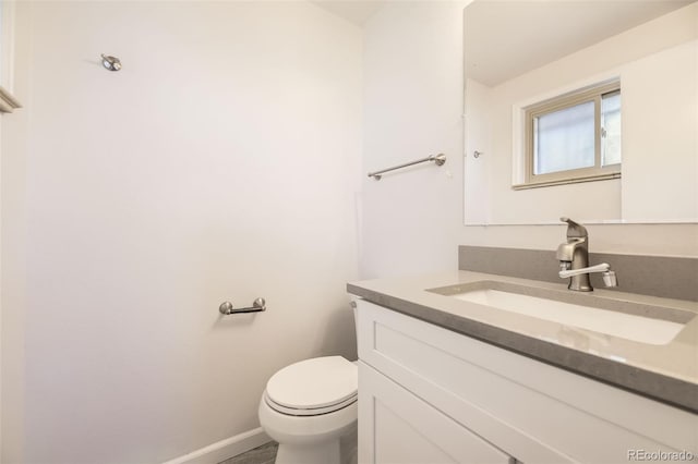 half bathroom with vanity, toilet, and baseboards