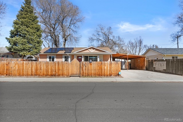 view of front facade with driveway, a fenced front yard, roof mounted solar panels, and a carport