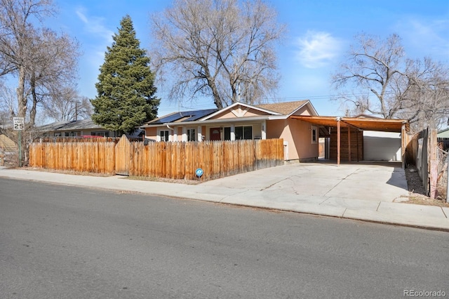 single story home with a fenced front yard, an attached garage, driveway, roof mounted solar panels, and a carport