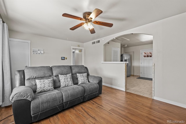 living room featuring arched walkways, visible vents, baseboards, and wood finished floors