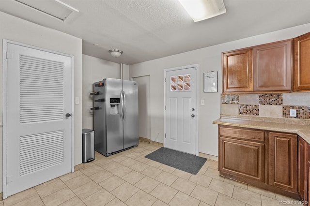 kitchen with brown cabinetry, decorative backsplash, stainless steel fridge with ice dispenser, light countertops, and a textured ceiling