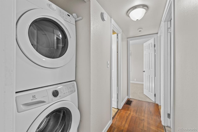 clothes washing area with stacked washer / drying machine, visible vents, wood finished floors, laundry area, and baseboards