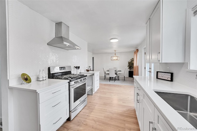 kitchen with white cabinetry, wall chimney range hood, stainless steel range with gas cooktop, light hardwood / wood-style flooring, and pendant lighting