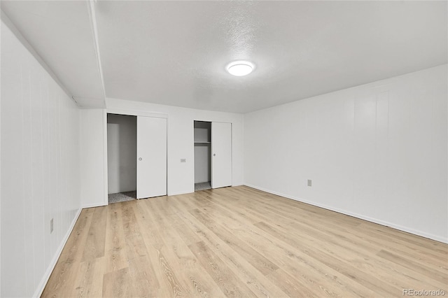 unfurnished bedroom with a textured ceiling, light wood-type flooring, and wood walls