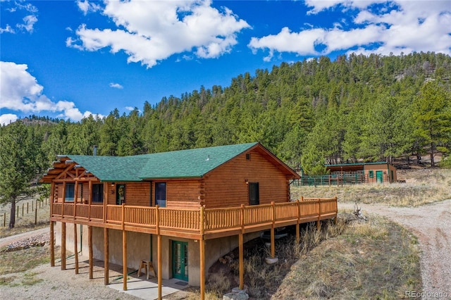 rear view of property with a wooded view, log exterior, and a deck