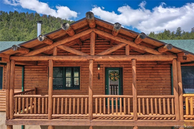 view of exterior entry with covered porch and a wooded view