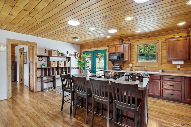 kitchen with a sink, black appliances, a kitchen breakfast bar, light countertops, and a center island