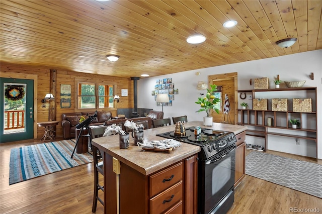 kitchen with black range with electric cooktop, a wood stove, a kitchen island, brown cabinetry, and light wood finished floors