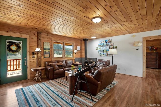 living room featuring a wood stove, wooden ceiling, wood finished floors, and wooden walls