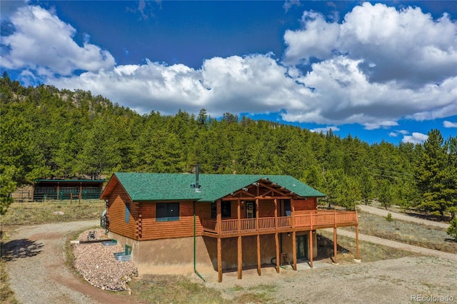 rear view of property featuring a wooded view, log exterior, a wooden deck, and dirt driveway