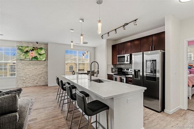 kitchen featuring sink, hanging light fixtures, light hardwood / wood-style flooring, an island with sink, and appliances with stainless steel finishes