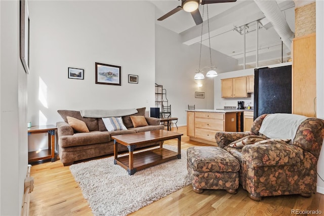 living room featuring a towering ceiling, light hardwood / wood-style floors, and ceiling fan