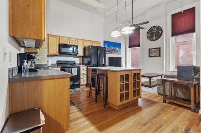 kitchen with a breakfast bar area, light hardwood / wood-style flooring, black appliances, a high ceiling, and sink