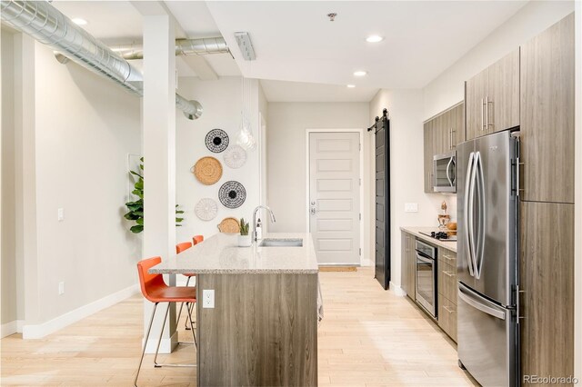 3198 Blake St Unit 402, Denver, CO 80205 - kitchen featuring stainless steel appliances, a barn door, light wood-type flooring, a kitchen breakfast bar, and recessed lighting
