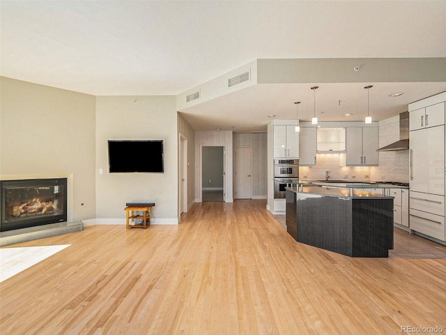 kitchen featuring wall chimney exhaust hood, stainless steel appliances, pendant lighting, light hardwood / wood-style floors, and a kitchen island