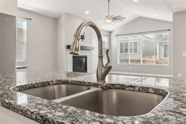 details featuring sink, white cabinetry, dark stone countertops, ceiling fan, and a tiled fireplace