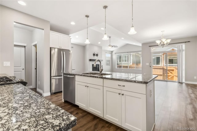 kitchen with sink, dark stone countertops, stainless steel appliances, white cabinets, and a center island with sink