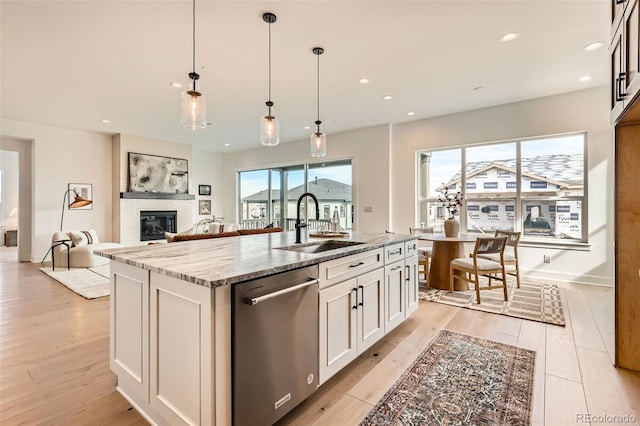 668 Leafy Aster Ln, Castle Rock, CO 80104 - kitchen featuring dishwasher, a sink, a glass covered fireplace, light stone counters, and light wood-type flooring