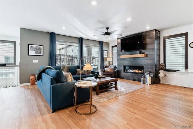 living room featuring ceiling fan, a large fireplace, and light wood-type flooring