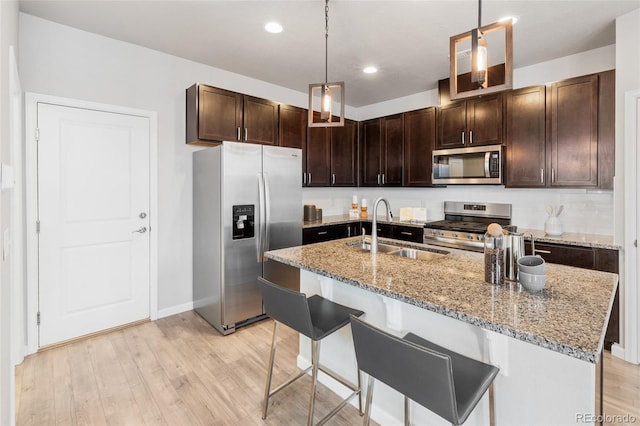 kitchen with stainless steel appliances, hanging light fixtures, sink, a breakfast bar, and light wood-type flooring