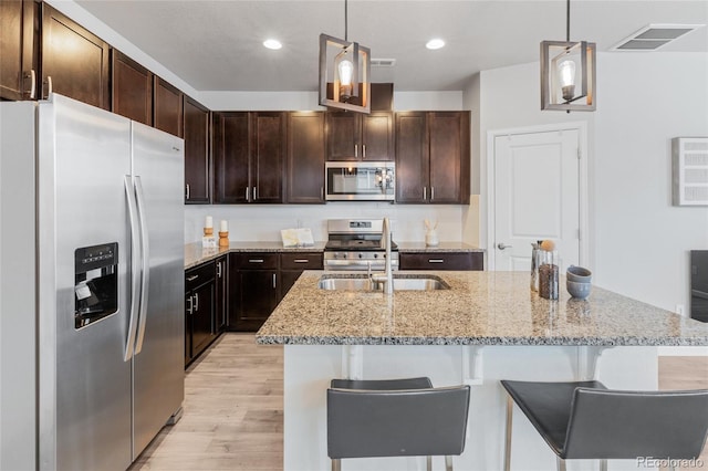 kitchen featuring sink, light wood-type flooring, appliances with stainless steel finishes, and decorative light fixtures