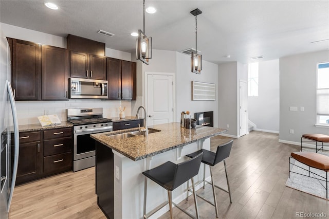 kitchen with stainless steel appliances, sink, a breakfast bar, an island with sink, and stone counters