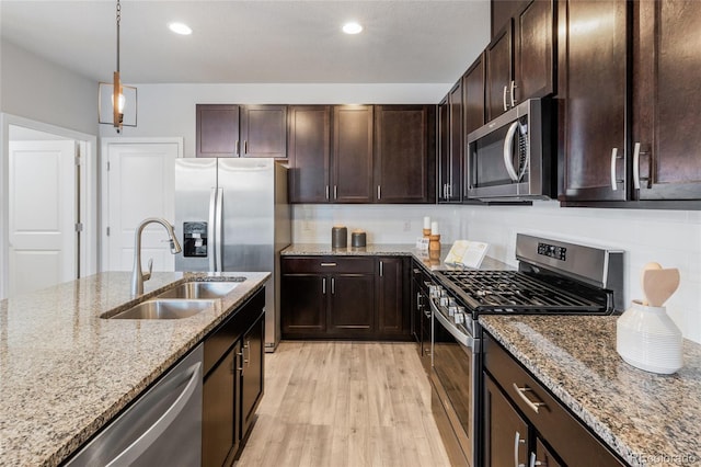 kitchen featuring stainless steel appliances, light hardwood / wood-style floors, sink, light stone countertops, and hanging light fixtures