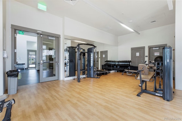 gym featuring a towering ceiling and light wood-type flooring