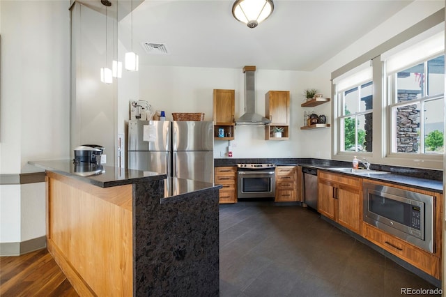 kitchen with appliances with stainless steel finishes, pendant lighting, sink, kitchen peninsula, and wall chimney exhaust hood