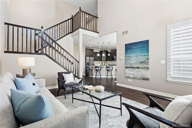 living room with dark wood-type flooring, a towering ceiling, and a wealth of natural light