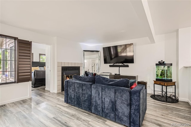 living area with baseboards, visible vents, a tiled fireplace, and wood finished floors