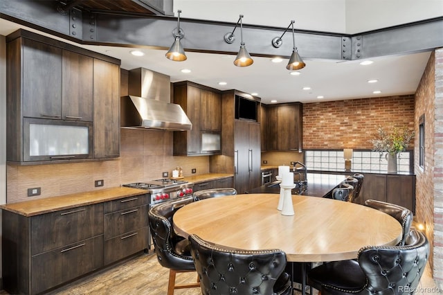 114 El Paso Blvd, Manitou Springs, CO 80829 - kitchen featuring wall chimney exhaust hood, dark brown cabinets, light wood-type flooring, backsplash, and brick wall