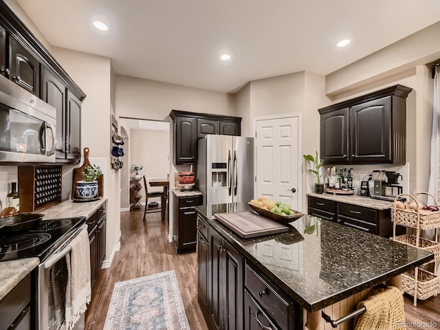 9412 Burgundy Cir, Highlands Ranch, CO 80126 - kitchen with appliances with stainless steel finishes, decorative backsplash, light wood finished floors, dark stone counters, and a center island