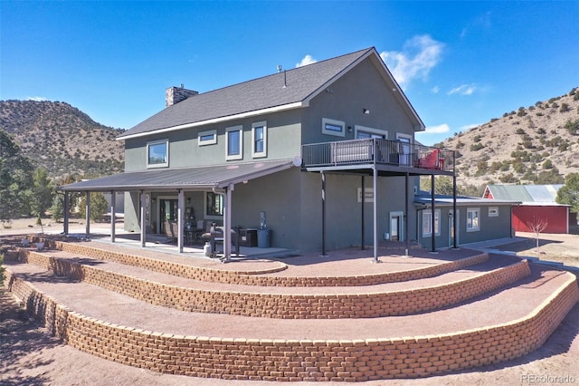 rear view of house featuring a chimney, metal roof, a patio area, a mountain view, and stucco siding