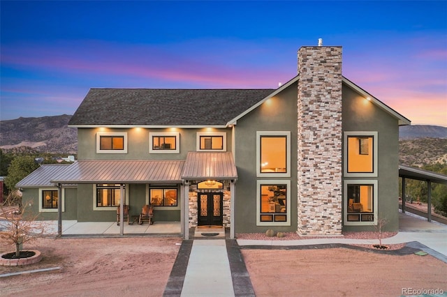 back of property featuring stone siding, a mountain view, metal roof, and stucco siding