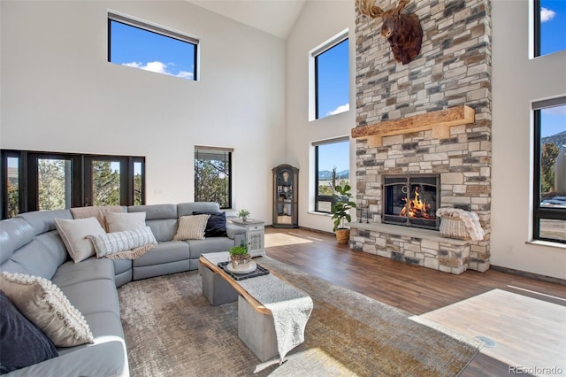 living area featuring baseboards, high vaulted ceiling, wood finished floors, and a stone fireplace