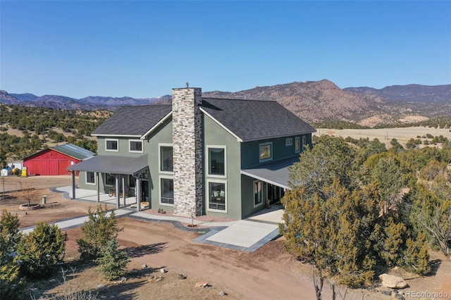 rear view of house with a chimney, dirt driveway, a mountain view, and stucco siding