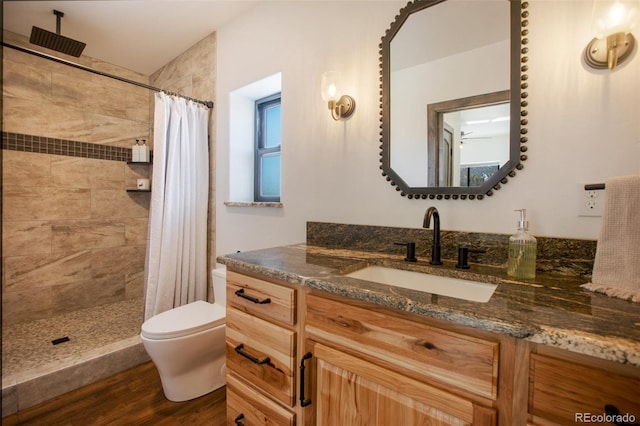 bathroom with a tile shower, vanity, toilet, and wood finished floors