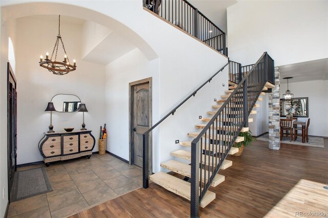 foyer entrance with baseboards, arched walkways, wood finished floors, a high ceiling, and a chandelier