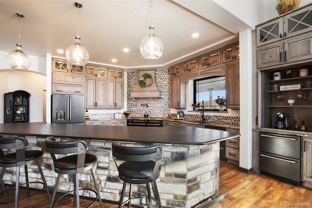 kitchen with dark countertops, backsplash, custom range hood, and stainless steel refrigerator with ice dispenser