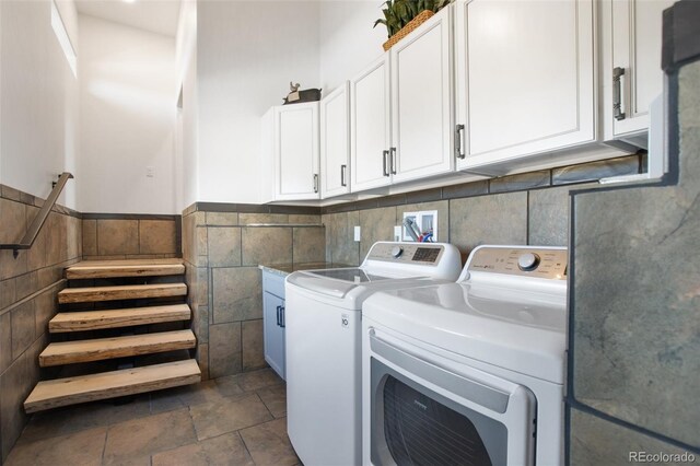 laundry room featuring a wainscoted wall, cabinet space, tile walls, and washing machine and clothes dryer