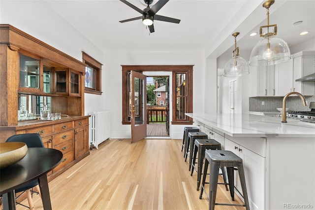 kitchen featuring radiator, light hardwood / wood-style flooring, light stone countertops, decorative light fixtures, and white cabinetry