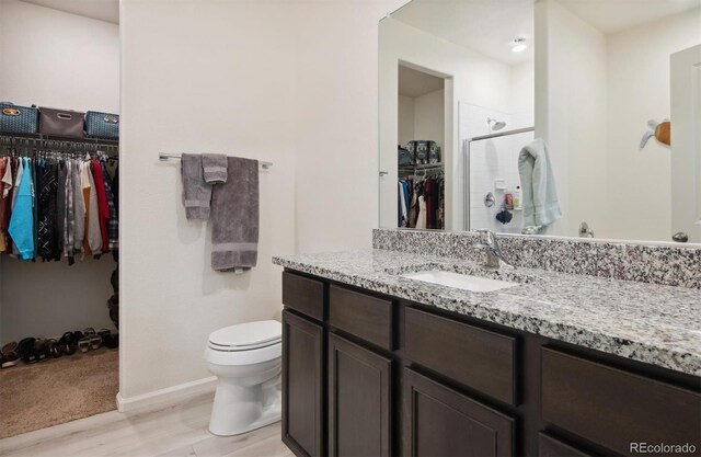 bathroom with a shower with door, hardwood / wood-style flooring, vanity, and toilet