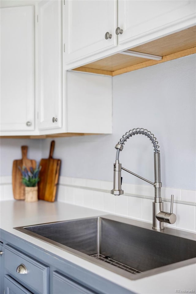 interior details featuring blue cabinets, white cabinets, a sink, and light countertops