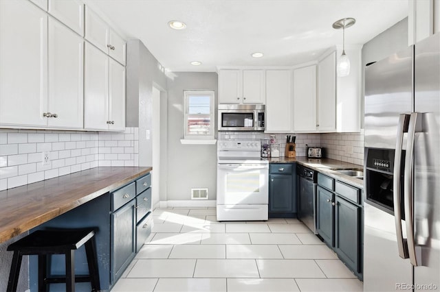 kitchen featuring butcher block counters, white cabinetry, light tile patterned floors, appliances with stainless steel finishes, and pendant lighting