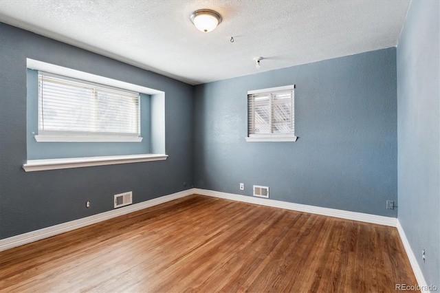 spare room with a textured ceiling, wood-type flooring, and a healthy amount of sunlight