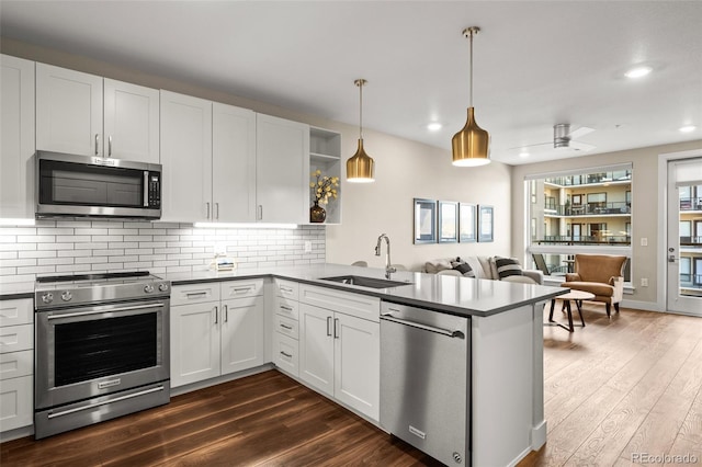 kitchen featuring appliances with stainless steel finishes, dark countertops, open shelves, a sink, and a peninsula