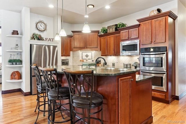 kitchen with appliances with stainless steel finishes, a center island with sink, light wood-type flooring, and decorative light fixtures