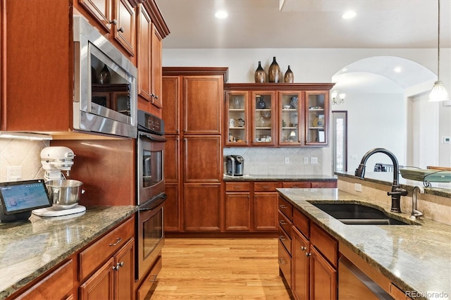 kitchen featuring sink, hanging light fixtures, stainless steel appliances, light stone countertops, and light wood-type flooring